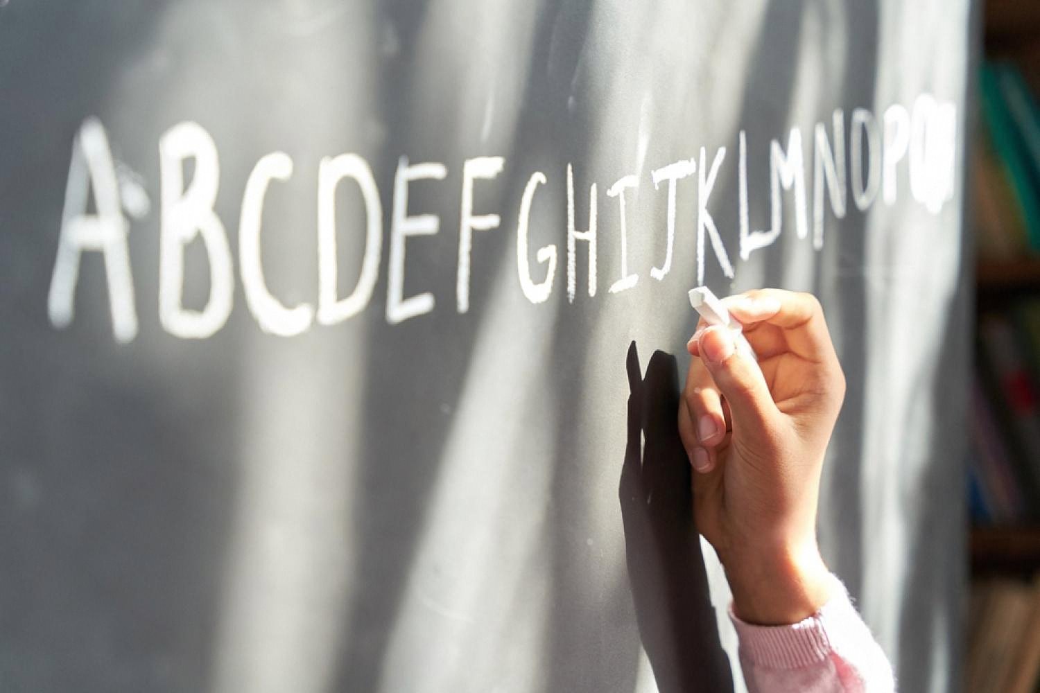 Hand writing the English alphabet on a chalkboard during an English lesson